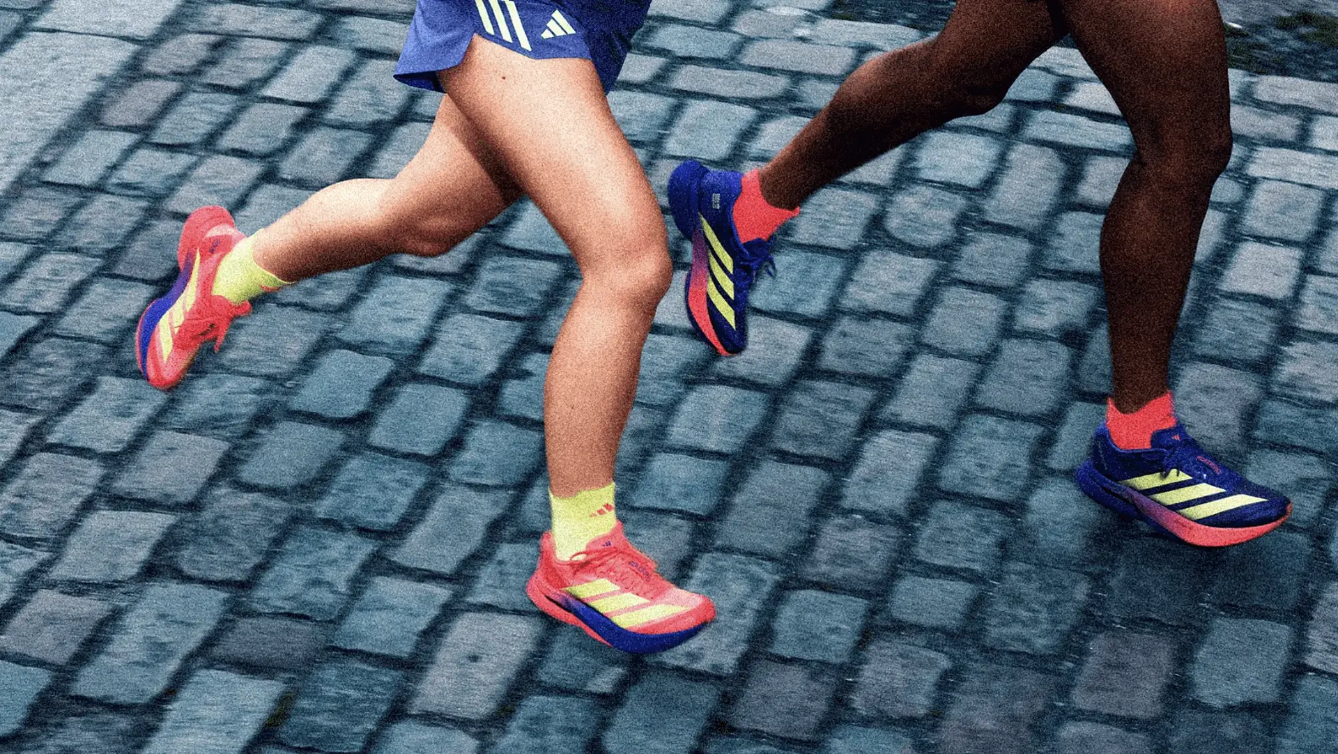 Zwei Läufer:innen in unterschiedlichen Schuhen der adidas Marathon-Kollektion rennen über Pflasterstein. Zu sehen sind nur die Beine.