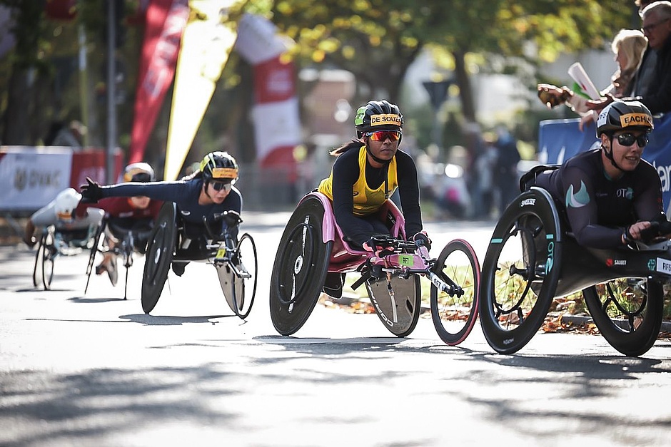 Athletes from various ethnic backgrounds competing in racing wheelchairs, one of them pink.