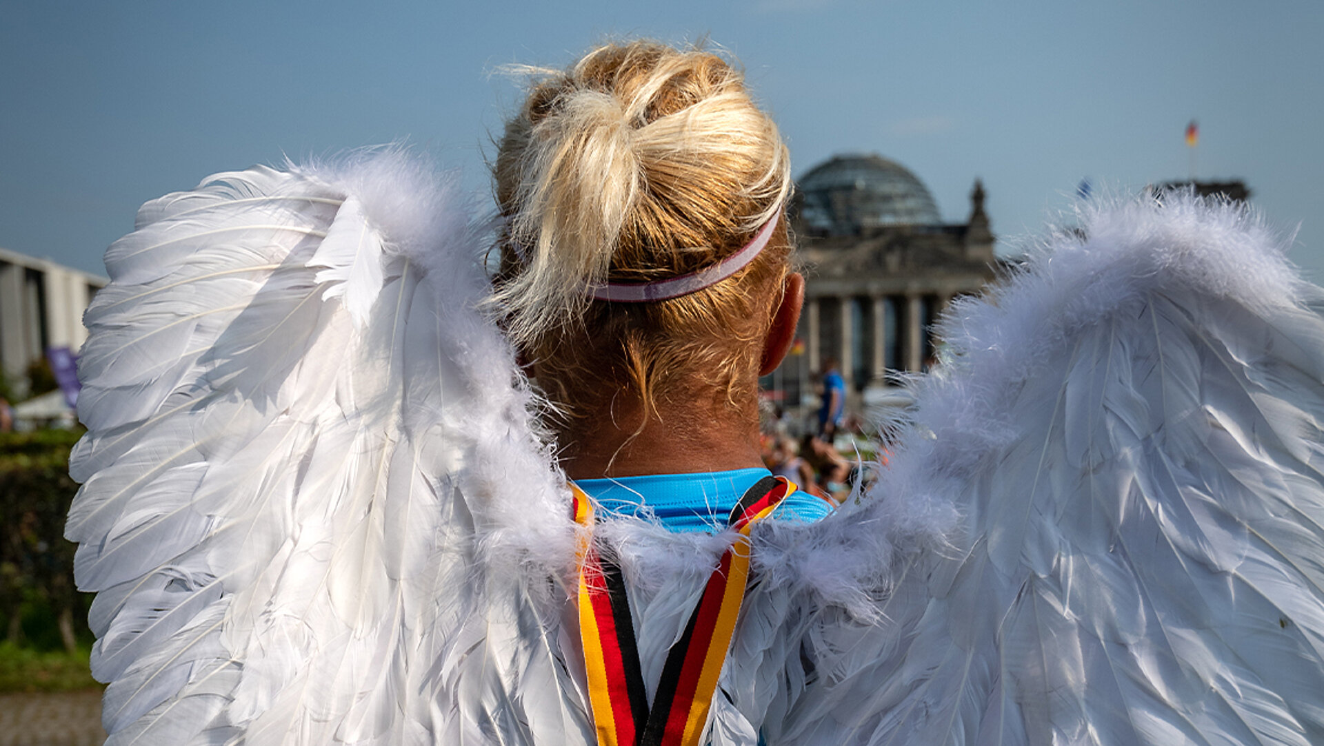 Läufer:in mit Engelsflügeln schaut auf den Berliner Reichstag.