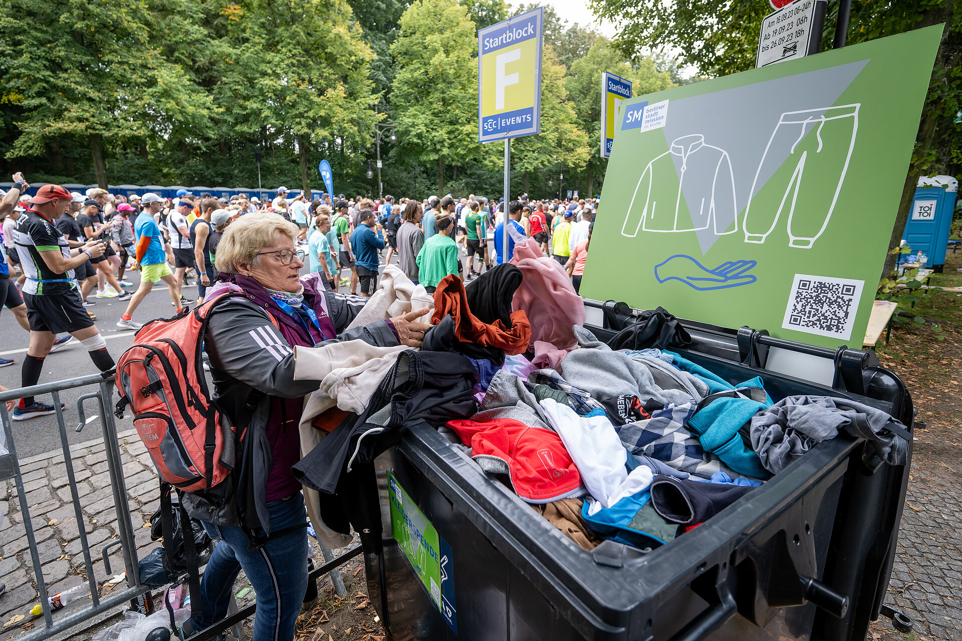 A woman is putting clothes into a collection bin belonging to the Berlin City Mission that is already full to the brim.