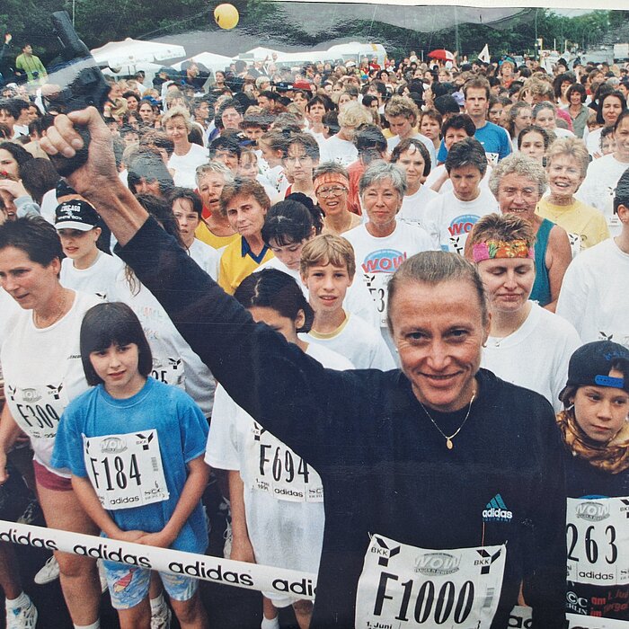 Grete Waitz raises the starting pistol in the air in front of the starting field of a race.