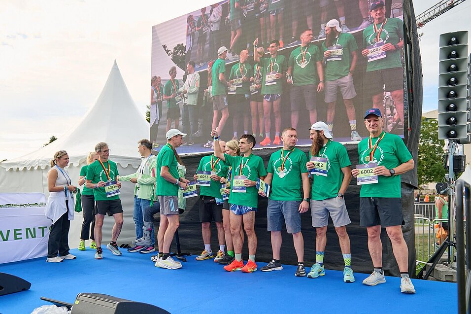 A handful of new Jubilees in green Jubilee shirts are standing on stage. On the far left is Irina Mikitenko, offering her congratulations.