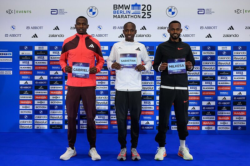 From left to right: Gabriel Gerald Geay, Sabastian Sawe, and Milkesa Mengesha hold up their race numbers for the camera.
