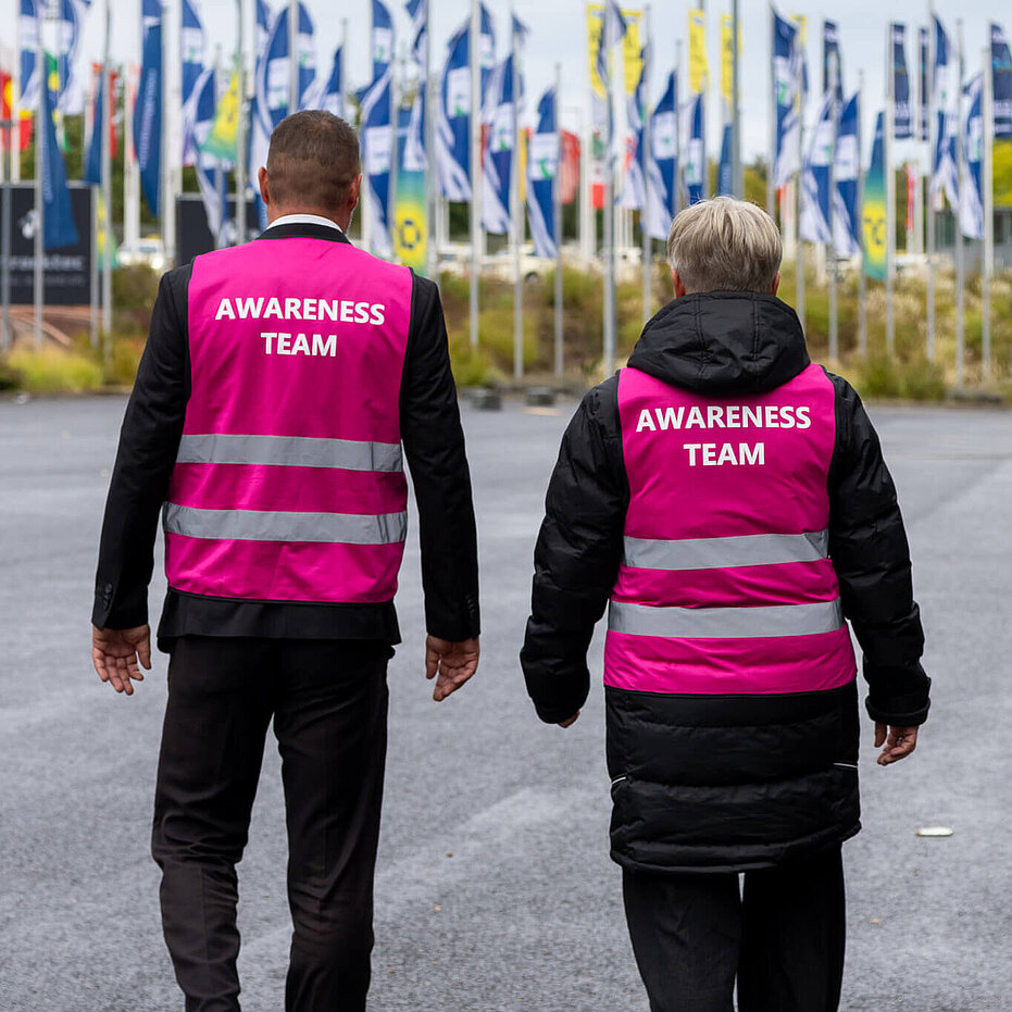 A man and a woman wearing pink safety vests with “Awareness Team” written on the back.